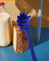 Close up of a GIR Spaghetti Spoon resting on a block of cheese next to a bottle of milk. 
